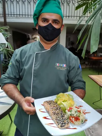 Joel Pinheiro de dólmã apresentando prato de peixe empanado em gergelim